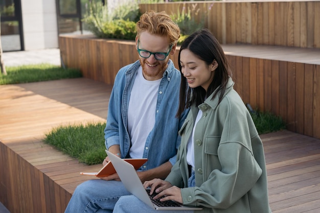 Smiling multiracial students using laptop computer studying together in university campus