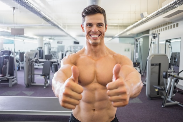 Smiling muscular man giving thumbs up in gym