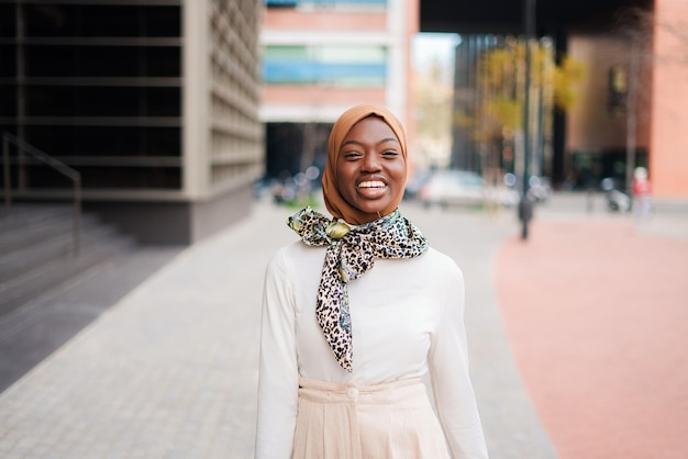 Smiling muslim black woman in hijab standing near office building