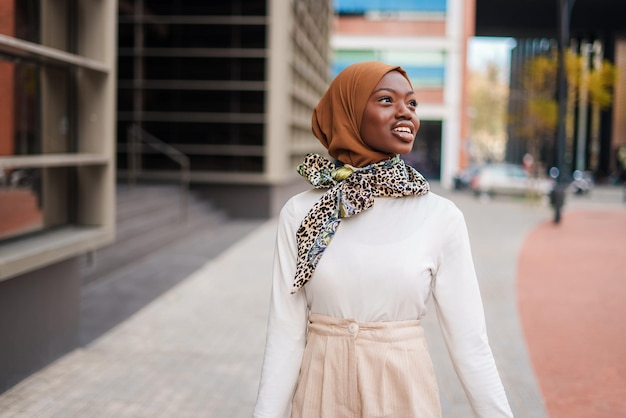 Smiling muslim black woman in hijab standing near office building