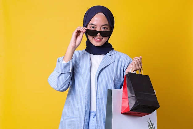 Smiling Muslim girl hold bags take off spectacles wear blue shirt and black veil