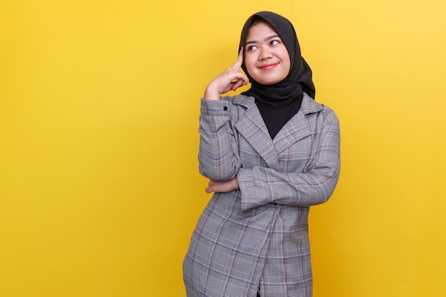 Улыбающаяся мусульманка в хиджабе с интересом смотрит на пространство для копирования и думает о чем-то Азии