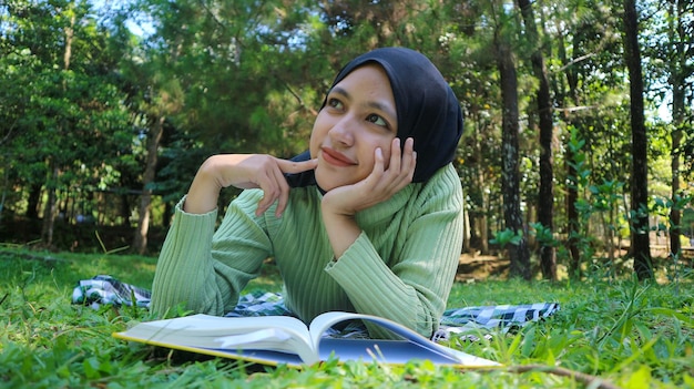 Smiling muslim woman in hijab in park holding book and pen thinking ideaEmpty space