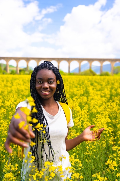 Smiling in nature a girl of black ethnicity with braids a traveler in a field of yellow flowers