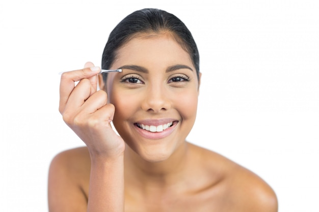 Smiling nude brunette using tweezers