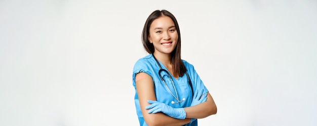 웃는 간호사 의료 종사자는 흰색 배경 위에 서 있는 covid19에서 패치를 사용하는 백신을 사용하여 팔을 보여주는 가슴에 팔을 교차합니다.