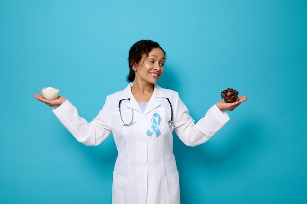 Smiling nutritionist in medical gown an blue ribbon holding a bowl with refined white sugar in one hand and ripe sweet dates in the other. Sugar and diabetes concepts for World Diabetes Awareness Day