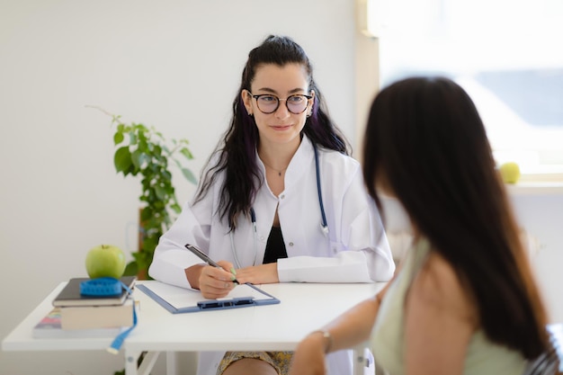 Foto nutrizionista sorridente che incontra un paziente in ufficio dietista che prescrive il trattamento che scrive il piano alimentare nel taccuino