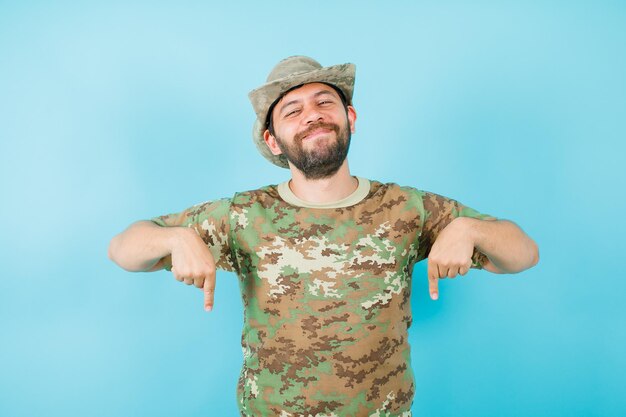 Smiling officer is pointing down with forefingers on blue background