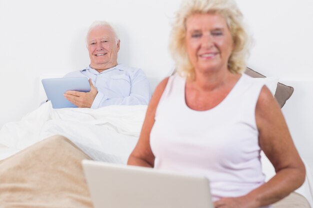 Smiling old couple using a tablet and the laptop