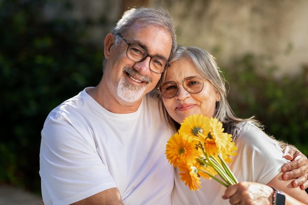 Smiling old european man and woman hugging with bouquet of flowers celebrating anniversary holiday