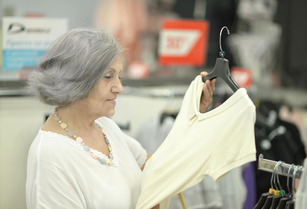 Smiling old lady choosing dress in store