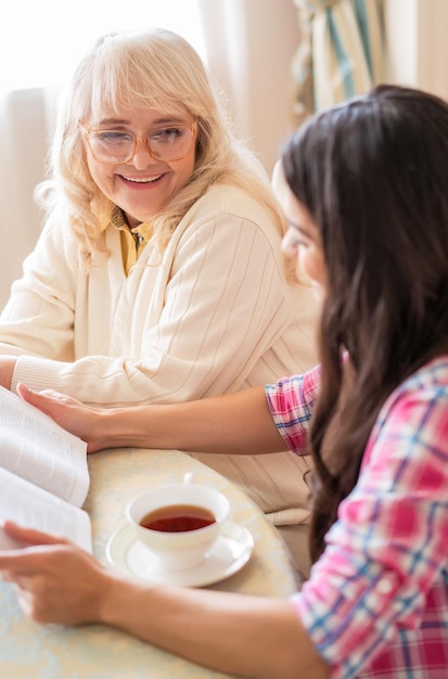 眼鏡をかけた笑顔の老婆は、お茶を飲みながら大声で読み上げる魅力的な娘の話を聞く時間を楽しんでいます