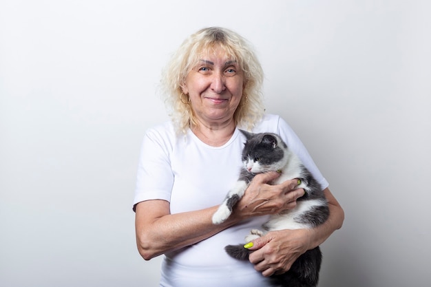 Smiling old woman holding a cat in her arms on a light background.