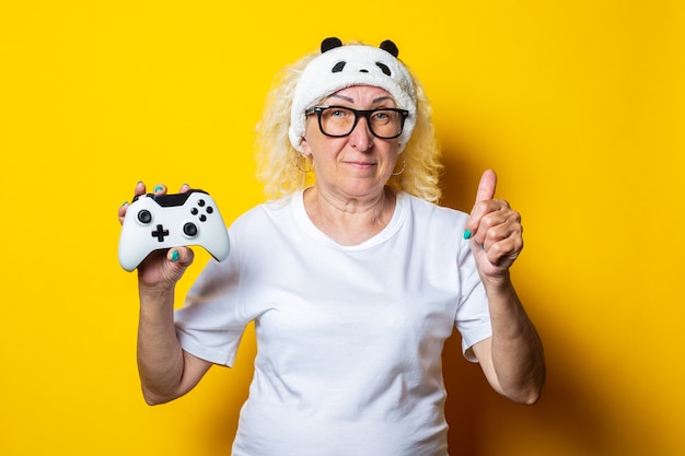 Smiling old woman with joystick in sleep mask shows thumb up hand gesture