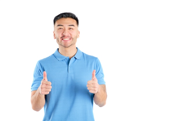 写真 青いポロシャツを着た笑顔の東洋の若い男が白い背景に親指を上げて正面を向いている