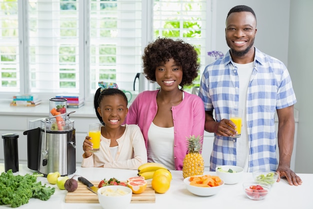 Smiling parents and daughter having a glass of orange juice in kitchen