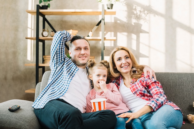 Photo smiling parents and daughter watching television sitting on sofa