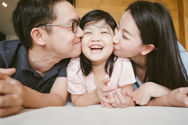 Photo smiling parents kissing daughter while relaxing on bed at home