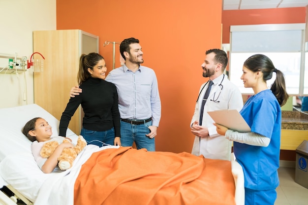 Smiling parents listening to healthcare workers while standing by sick daughter at hospital