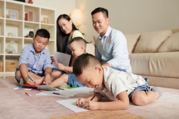 Smiling parents looking at their three sons drawing pictures on floor