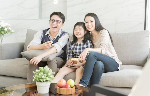 Smiling parents sitting with daughter on sofa in living room at home