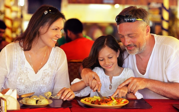 Smiling parents teaching their daughter to use knife in cafe