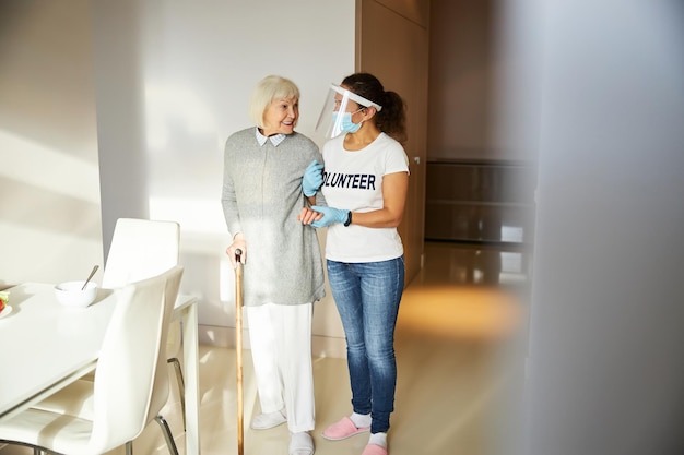 Photo smiling pensioner looking at her caregiver in a face shield