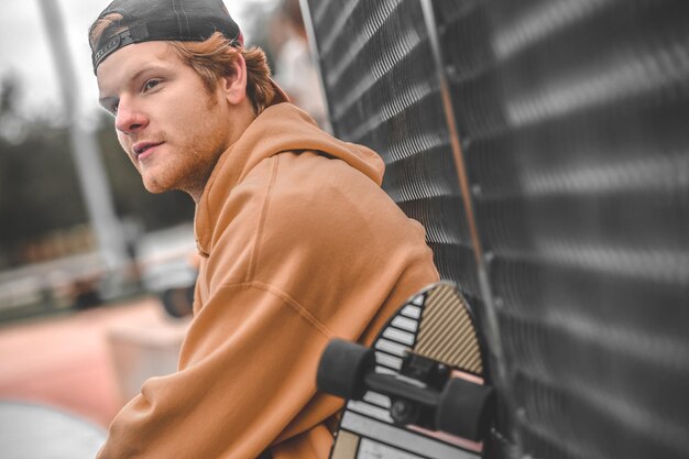 Smiling pensive guy having rest near skateboard outdoors