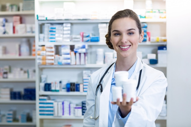 smiling pharmacist showing medicine container in pharmacy