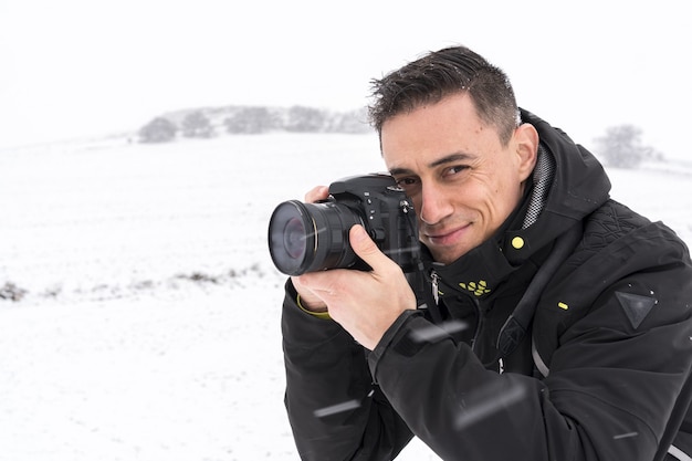 寒い冬の日に雪景色で写真を撮る笑顔の写真家
