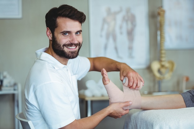 Smiling physiotherapist putting bandage on injured feet of patient