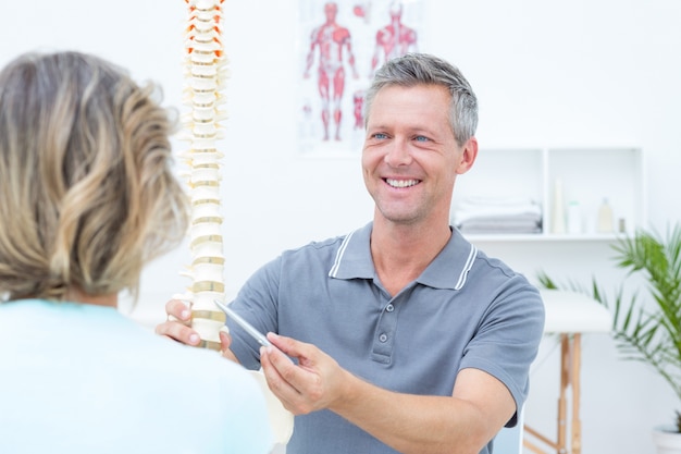 Smiling physiotherapist showing spine model to his patient