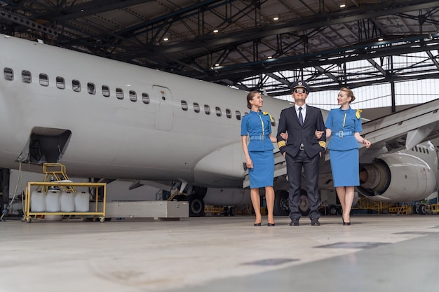 Smiling pilot and flight attendants walking through the hangar together