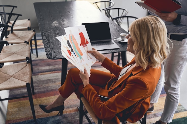 Smiling pleased blonde young Caucasian fashion designer working in a studio with her male colleague