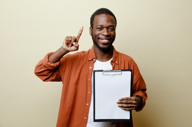 smiling points at up young african american male holding clipboard isolated on white background