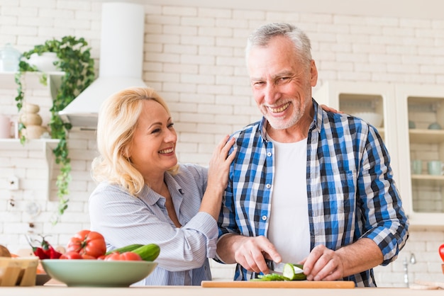 Ritratto sorridente delle coppie senior che preparano alimento nella cucina