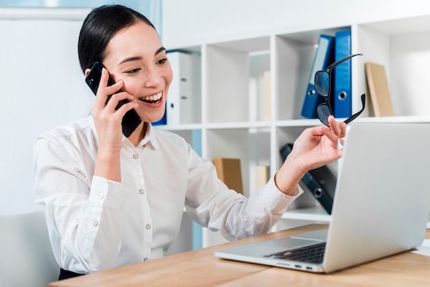 Foto ritratto sorridente di giovane donna di affari che parla sul telefono cellulare che esamina computer portatile