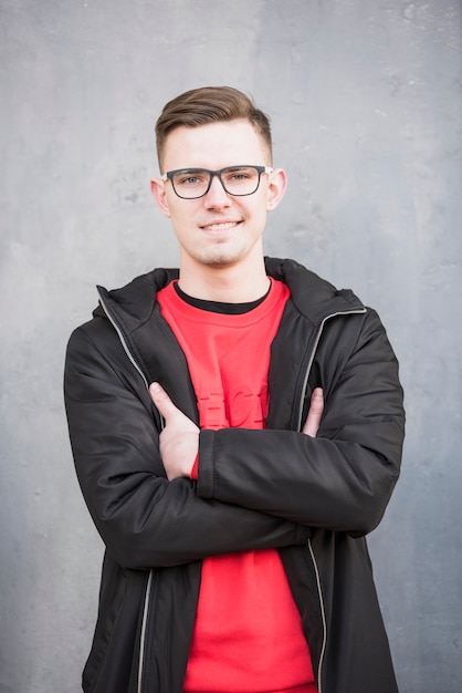 Smiling portrait of a young man wearing black jacket with his arms crossed against concrete backdrop