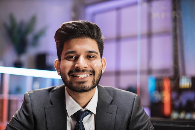 Smiling positive confident indian man in formal wear sitting at
office desk