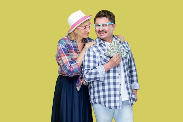 Smiling positive couple of friends standing together man holding fan of dollar banknotes