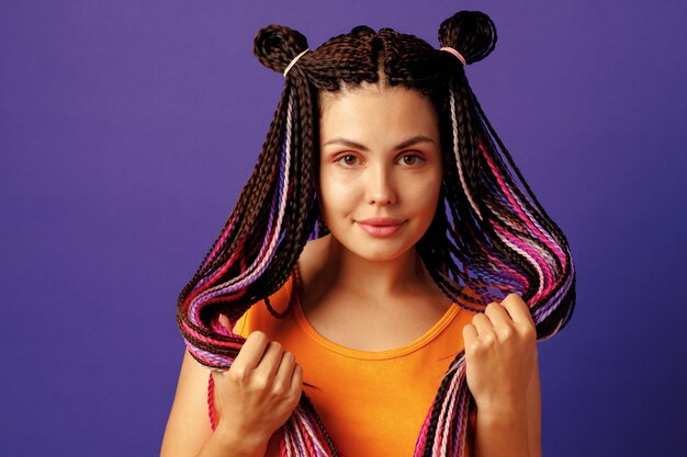 Улыбающаяся позитивная молодая женщина с красочными африканскими косами на фиолетовом