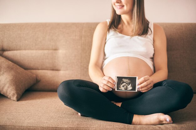 Smiling pregnant lady keeping ultrasound image of baby