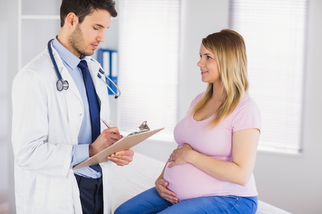 Photo smiling pregnant patient talking to doctor which is taking notes