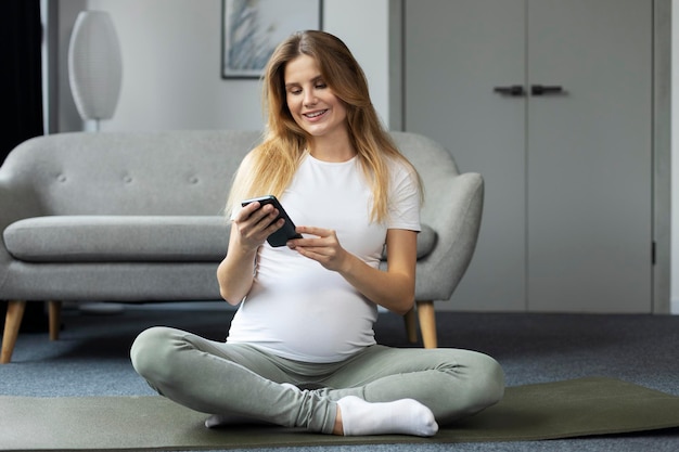 Smiling pregnant woman holding smartphone using mobile app watching video sitting at home