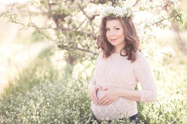 Smiling pregnant woman making heart with fingers in meadow Looking at camera Motherhood Maternity 20s