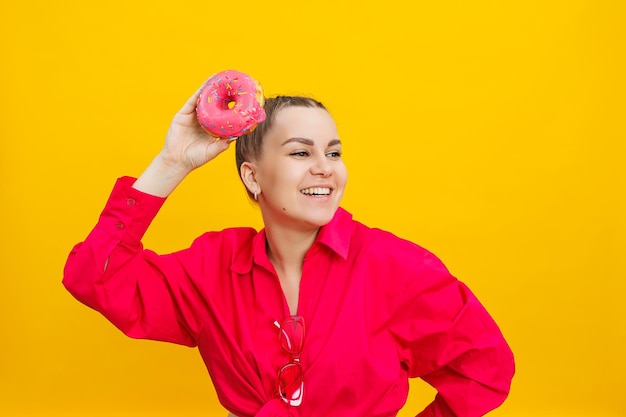 Smiling pregnant woman in pink shirt holding delicious sweet donuts on isolated yellow background sweet caloric food during pregnancy a pregnant woman eats fatty pastries