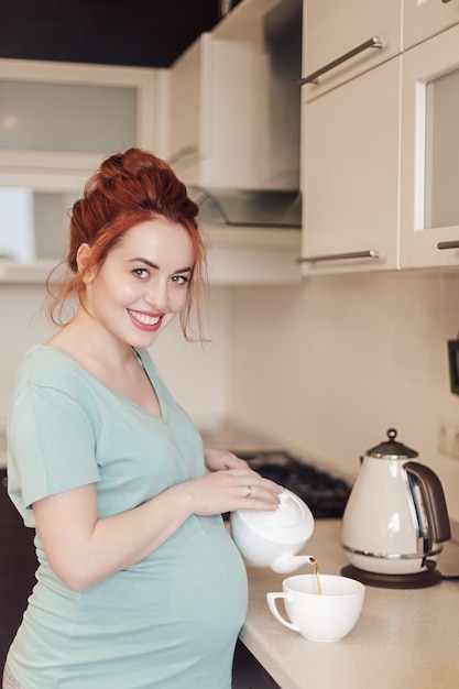 Smiling pregnant woman pouring tea