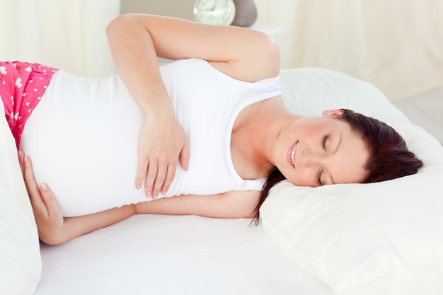 Smiling pregnant woman resting in her bed in the bedroom