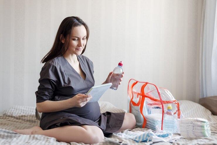 Smiling pregnant woman sitting on the bed with a list in his hands, collects things in a bag for the hospital